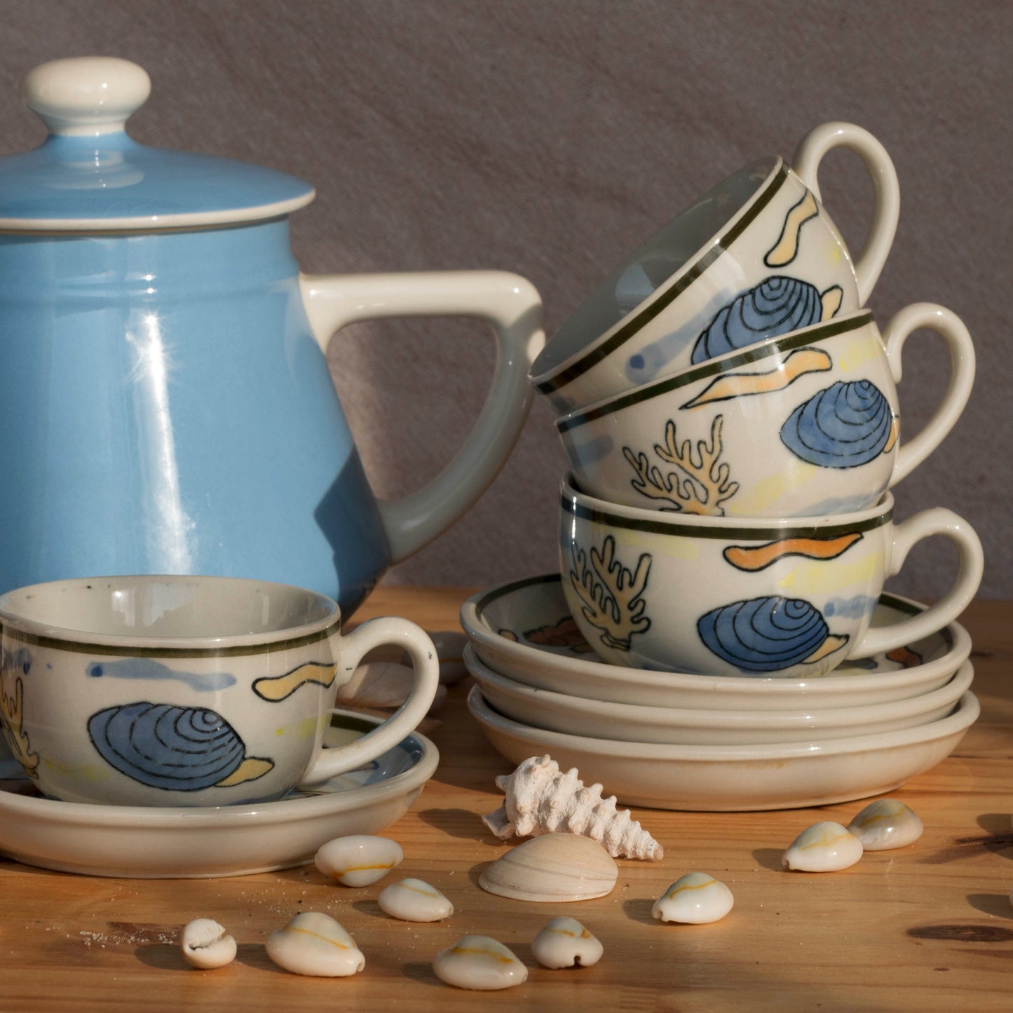 Tasse coquillage Second Joy avec soucoupe, posée sur un décor marin avec sable, collection Vent d’Été, Havre.